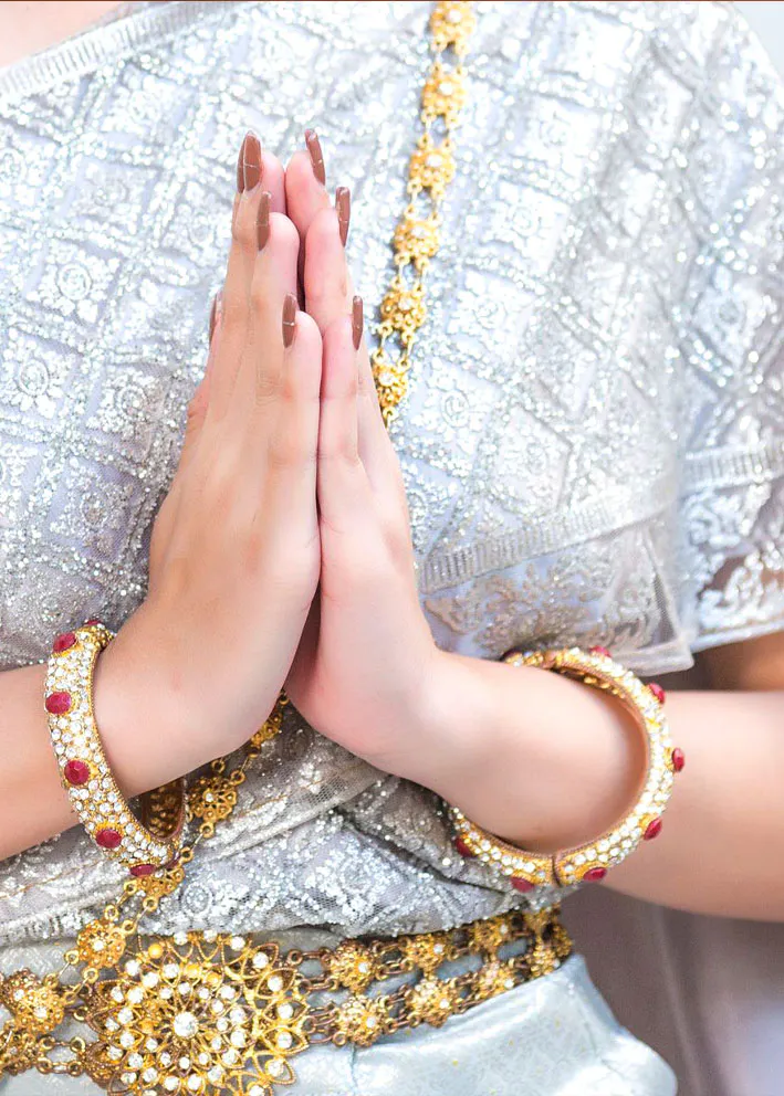 Hands raised in a wai, wearing traditional Thai gold jewelry