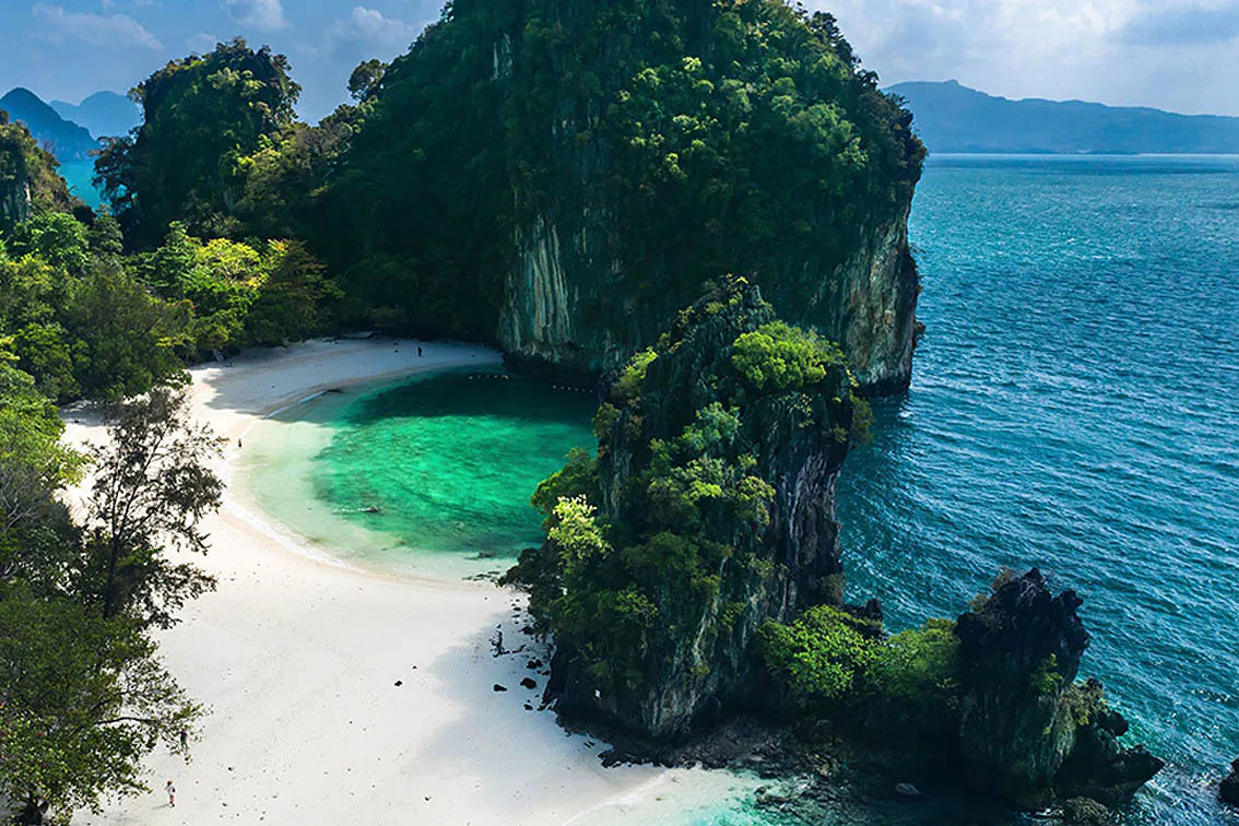 Aerial view of a white-sand cove framed by limestone cliffs and emerald water in Krabi