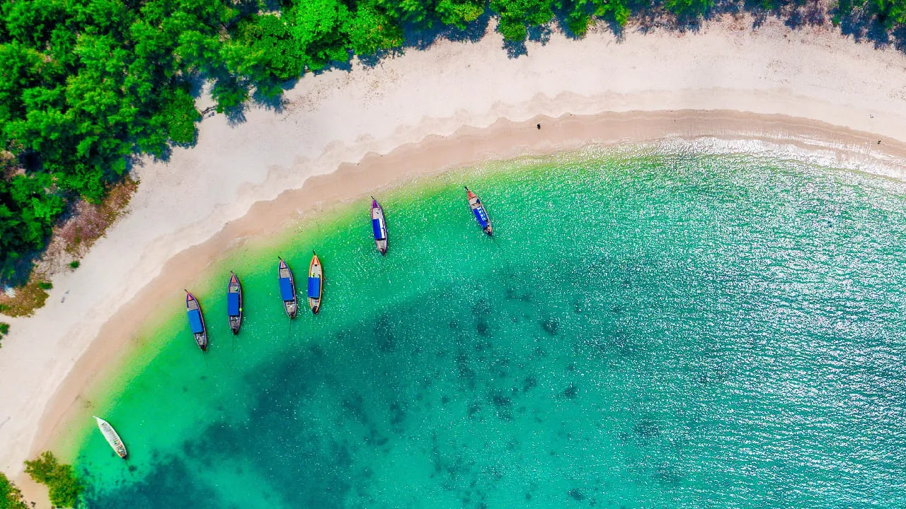 Aerial view of a crescent white-sand bay with traditional long-tail boats in turquoise water