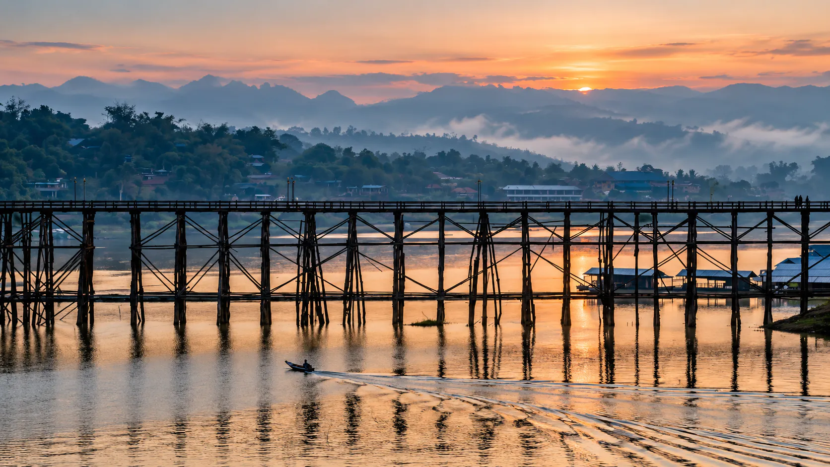 Mon Bridge stretching across misty mountain waters at sunrise in Sangkhlaburi
