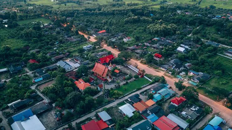 Aerial view of a temple and village nestled in lush western Thailand countryside at golden hour